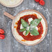 An American Metalcraft round pizza peel with a pizza topped with sauce and basil leaves.