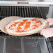 A person using an American Metalcraft pizza peel to put a pizza in the oven.