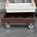 A person using a Cambro dark brown pizza dough box dolly to hold a white container.