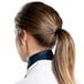 A woman in a white lab coat and a ponytail wearing a denim chef neckerchief.
