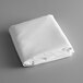 A folded white rectangular Intedge table cloth on a gray surface.