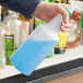 A hand holding a blue Off-Set Neck Molded Plastic bottle with a green label spraying over a black grate.