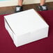A plain white, square bakery box with a closed lid, measuring 6 x 6 x 2.5 inches.