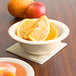 A bowl of orange slices on a table with a bowl of apples.