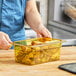 A woman holding a Carlisle amber plastic food pan filled with fried chicken on a counter.
