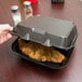 A hand holding a Genpak black foam container with food in it.