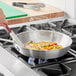 A person cooking food in a Choice aluminum fry pan on a stove.