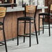 Three Lancaster Table & Seating black bar stools with black vinyl seats and natural wood backs at a bar counter.