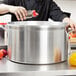 A person using a spice grinder to season a Vollrath Wear-Ever sauce pot.