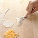 A person using an Ateco stainless steel circle cutter with a blue silicone handle to cut dough.