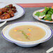 A Fineline white plastic bowl with blue and gold rim on a table with a bowl of soup and salad.