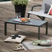 A Grosfillex Volcanic Black aluminum cocktail table on an outdoor patio with a glass of wine on it.