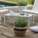 A white Grosfillex outdoor cocktail table on a patio with a plant.