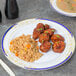 A Fineline white plastic dinner plate with blue and gold accents holding Chinese food on a table.