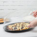 A hand putting food into a Fineline clear plastic tray with a clear plastic dome lid.