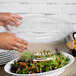 A person holding a clear plastic Fineline tray dome lid over a salad.