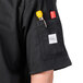 A close-up of a Mercer Culinary black chef jacket pocket with a pen and thermometer inside.