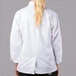 A woman wearing a Mercer Culinary white long sleeve chef jacket with cloth knot buttons.