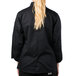 A woman wearing a black Mercer Culinary chef jacket with long sleeves and cloth knot buttons.