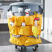 A Rubbermaid yellow trash can with cleaning supplies inside, including a white spray bottle and a bag of cleaning supplies.