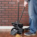 A person using a Rubbermaid angled lobby broom to sweep the floor.