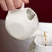 A hand pouring tea from a white Tuxton China teapot into a cup.