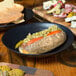 A hot dog in a black bowl next to a 10 Strawberry Street black stoneware plate filled with food.