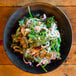 A bowl of salad on a 10 Strawberry Street black stoneware plate on a wood table.