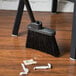 A black Carlisle Duo-Sweep lobby broom sitting on a wooden floor.