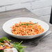 A white 10 Strawberry Street stoneware plate with a bowl of spaghetti and a fork.