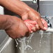 A person using a Cordova orange cooling towel to wash their hands in a sink.