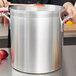 A person using a wooden spoon to stir a large Vollrath Wear-Ever stock pot.