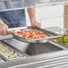 A man holding a Vollrath stainless steel oval pan full of shrimp on a buffet counter.