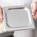 A person holding a silver square pan cover.