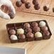 A person holding a brown 15-cavity candy tray filled with chocolate truffles.