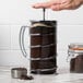 A person using a Libbey stainless steel French press to pour coffee on a counter.