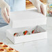 A person in gloves holding a white candy box with strawberries in it.