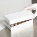 A gloved hand holding a white 7 3/8" x 4" x 1 1/8" candy box.