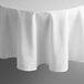 A white Intedge 83" round polyester table cover with a hemmed edge on a table.