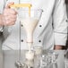 A person using a Matfer Bourgeat automatic dispenser funnel to pour white liquid into a glass.