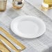 A Visions white plastic plate with a knife and fork on a napkin.