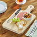 A wooden Choice cutting board with food on it, a knife, and a bowl of nuts and dried fruit.