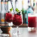 A wine glass filled with Monin Blueberry fruit puree and mint leaves with a bowl of blueberries on a table.