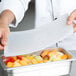 A chef using a Flexsil high-heat silicone lid to cover a tray of fruit.