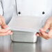 A person in a chef's uniform holding a white Flexsil high-heat silicone lid over a plastic container.