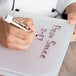 A hand using a brown and white Flexsil lid to write on a plastic container.