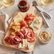 A Choice wooden bread and charcuterie cutting board with a handle holding meats and cheeses on a table.