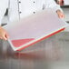 A chef using a Flexsil high-heat silicone lid on a plastic tray of red food.