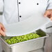 A person holding a Flexsil high-heat silicone lid on a tray of green beans.
