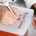 A hand writing on a brown and white Flexsil lid with a pen.